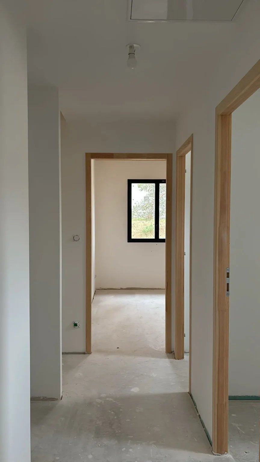 Couloir d'un bâtiment en construction avec plusieurs portes en bois ouvrant sur des pièces vides, dont une avec une fenêtre