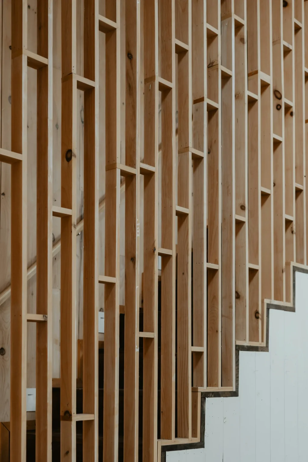 Claustra en bois clair avec des découpes rectangulaires, longeant un escalier blanc.