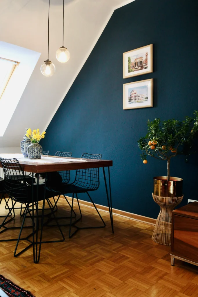 Salle à manger avec mur bleu nuit, table en bois, chaises métalliques et un chat sur la table.