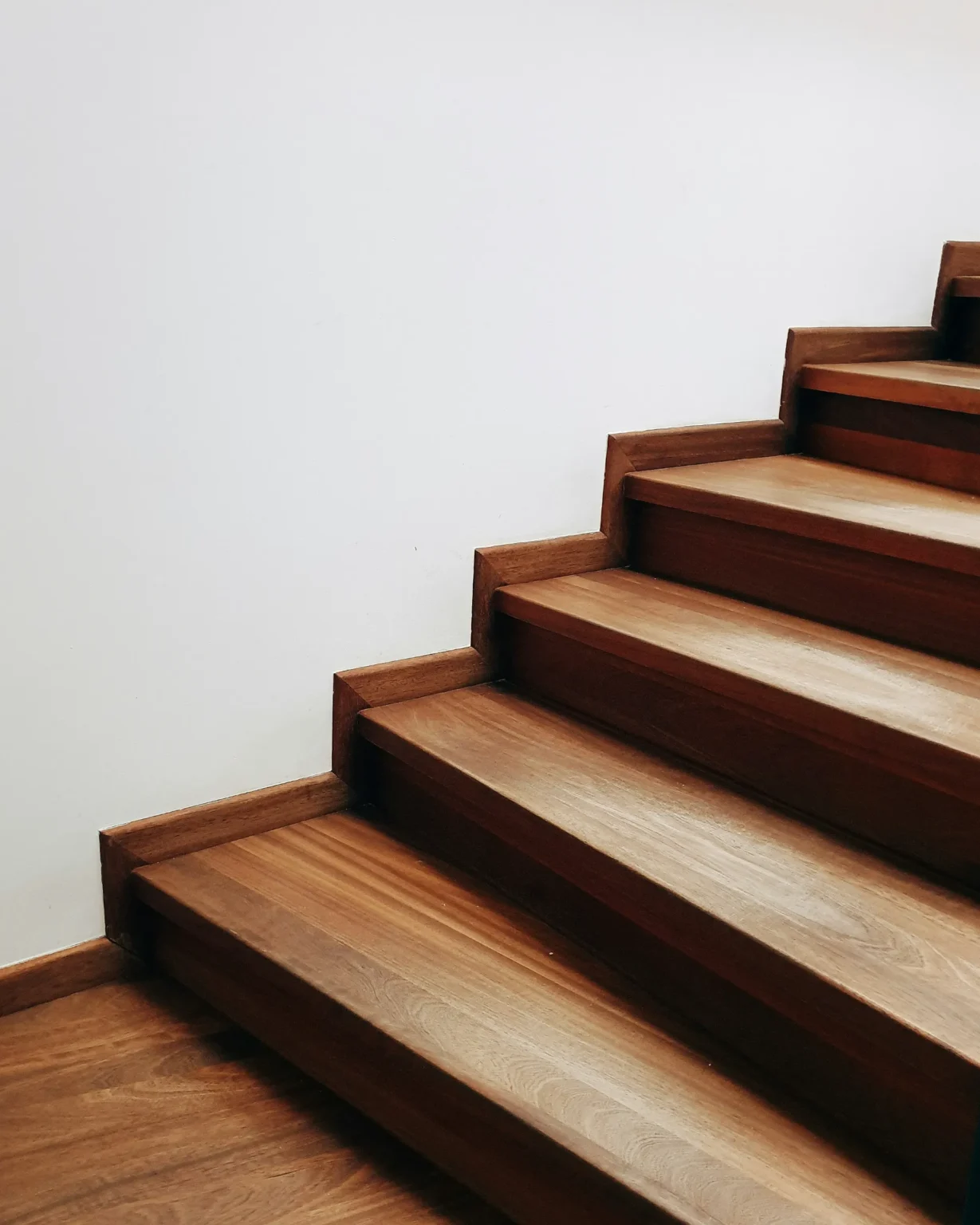 Escalier moderne en bois brun, avec des marches serrées et un mur blanc épuré.