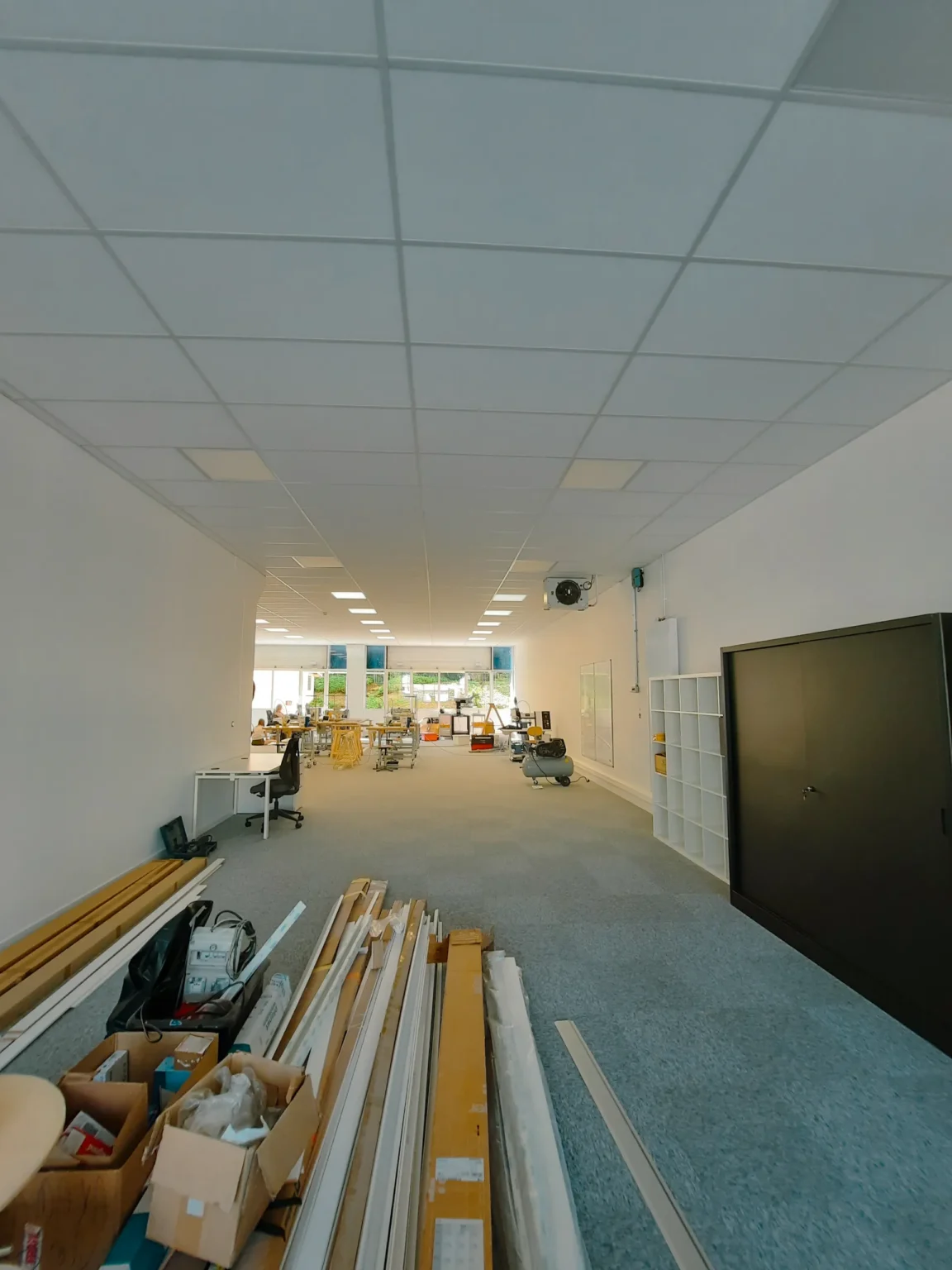 Bureau lumineux en cours d'aménagement avec du matériel de construction au premier plan, des bureaux et des étagères au fond.