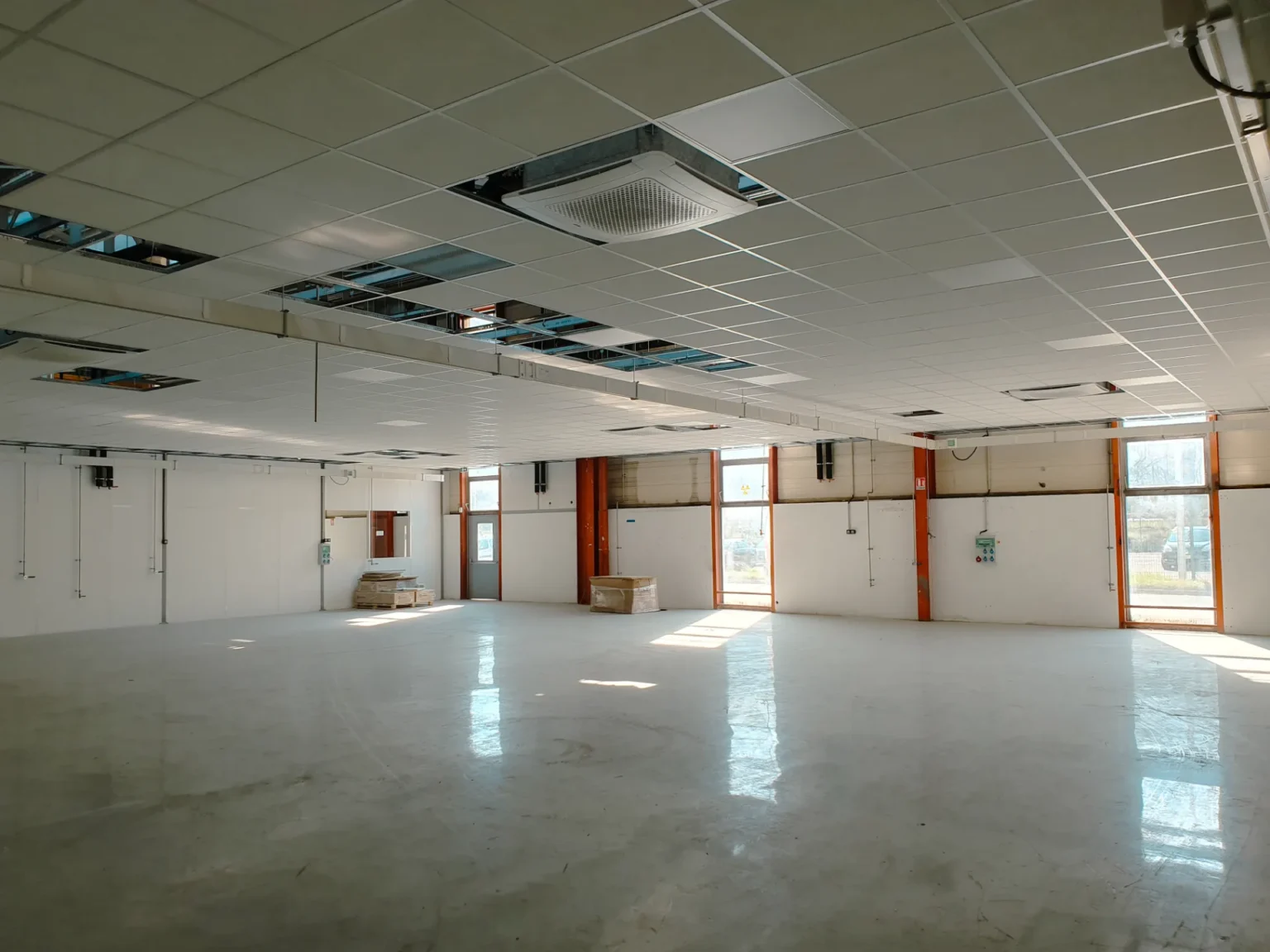 Intérieur lumineux d'un espace professionnel avec sol en béton poli et faux plafond modulaire partiellement ouvert.