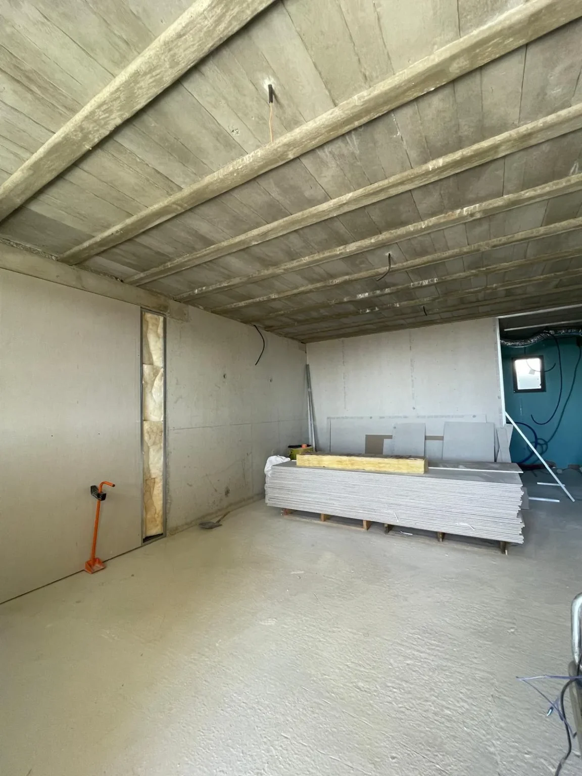 Chantier intérieur avec un plafond en poutres apparentes, murs en plaques de plâtre, tas de plaques de plâtre et isolant