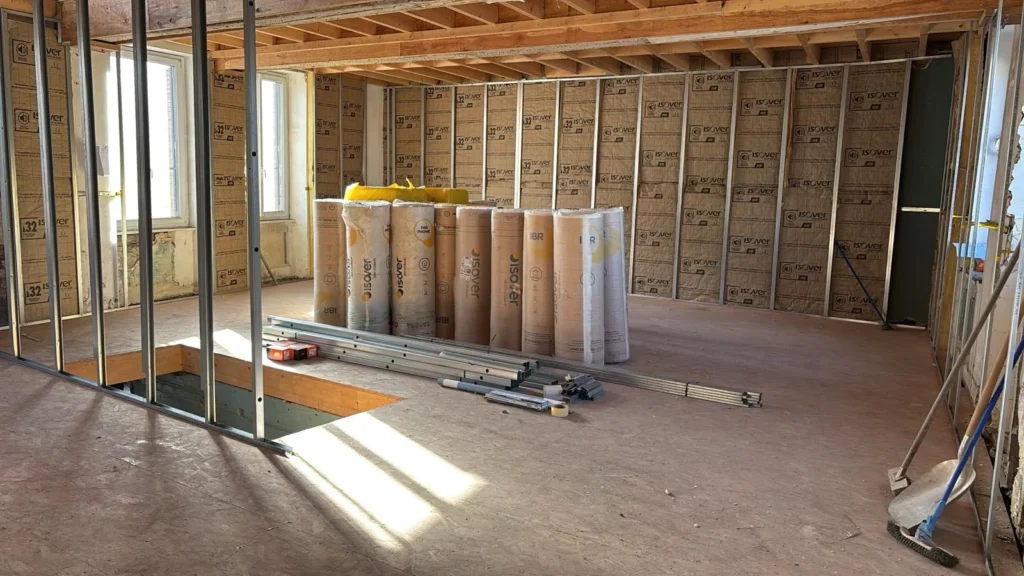 Un chantier intérieur avec murs isolés, rouleaux d'isolant et matériaux de construction au sol.