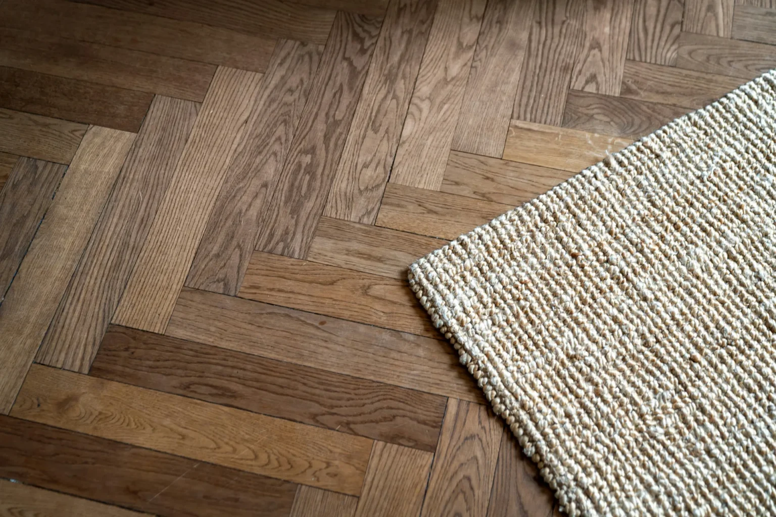 Un tapis en jonc tressé est posé sur un parquet en bois motif chevrons