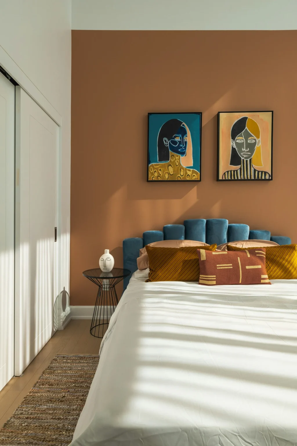 Lit avec tête de lit bleue, coussins dorés et un tableau abstrait de deux visages