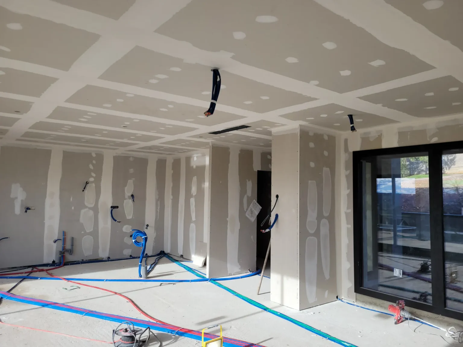Chantier intérieur : murs et plafond en plaques de plâtre, apparents, avec câbles électriques et tuyauterie au sol.