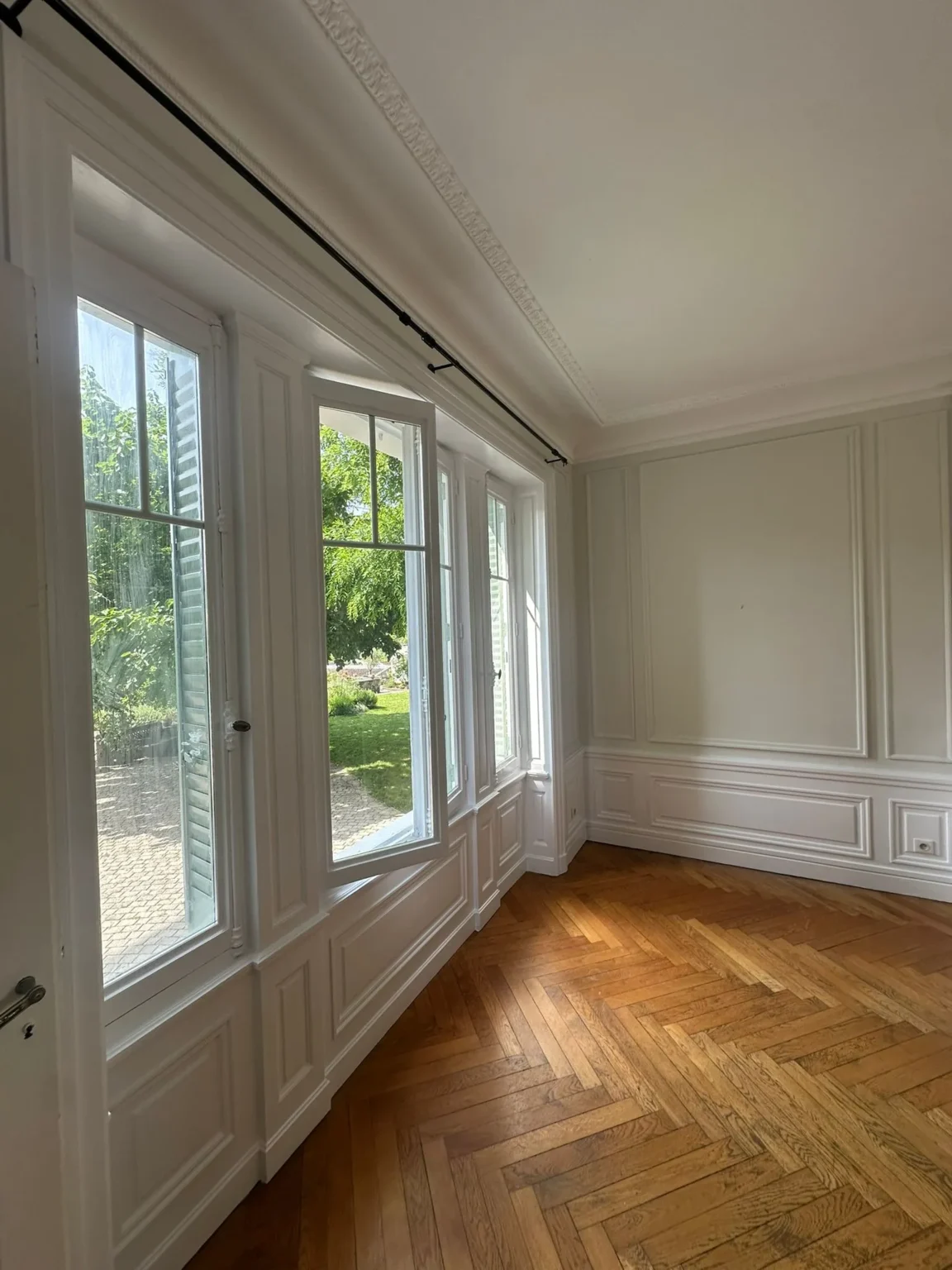 Pièce lumineuse avec de grandes fenêtres donnant sur un jardin verdoyant et un parquet en chevrons