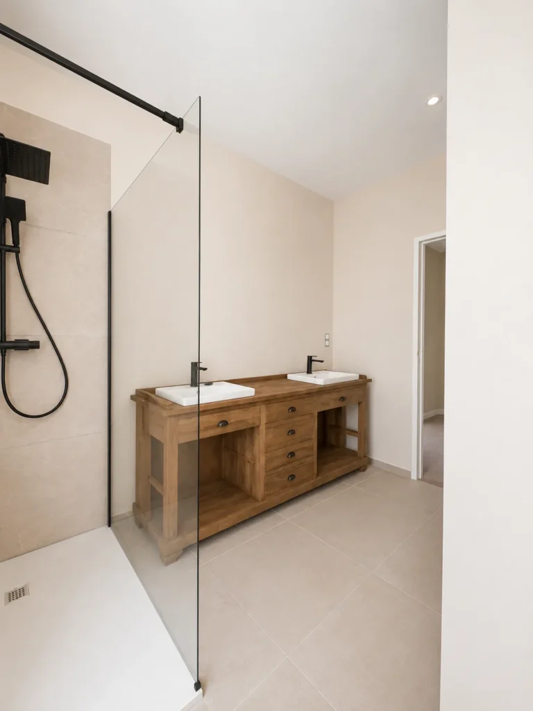 Salle de bain moderne avec douche à l'italienne, meuble double vasque en bois et robinetterie noire.