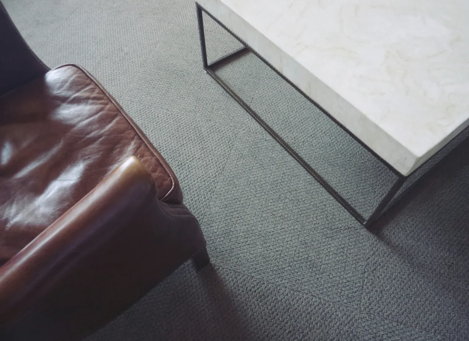 Un fauteuil en cuir marron et une table basse rectangulaire avec un plateau en marbre clair sur un tapis gris