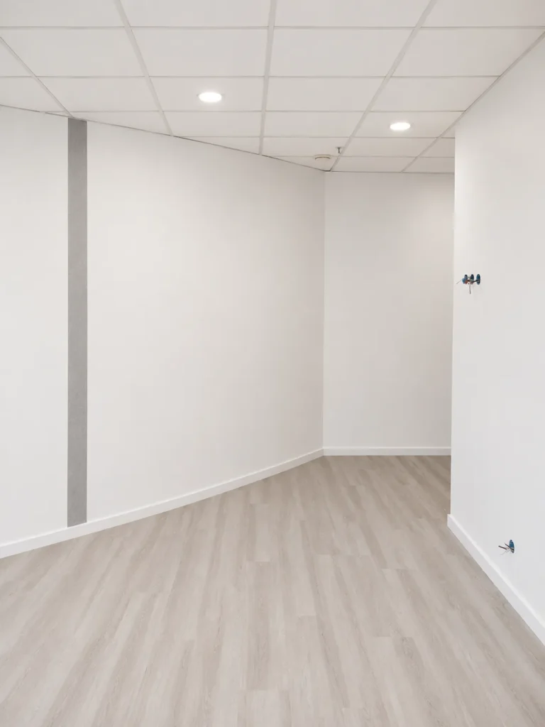 Intérieur d'un bureau lumineux avec un sol en parquet stratifié clair, des murs blancs et un plafond suspendu à carreaux avec des spots encastrés.
