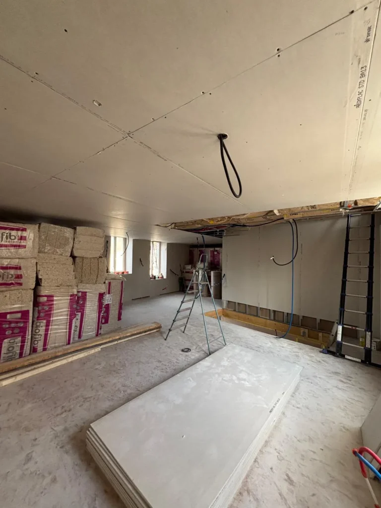 Chantier de construction avec plaques de plâtre, isolant et échelle dans une pièce en cours d'aménagement.